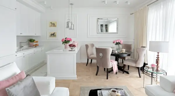 Elegancki salon z kuchnią inspiracje: białe meble, beżowe krzesła, okrągły stół, lustro, obrazy z końmi, kwiaty.