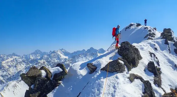 Wspinaczka na Orlą Perć zimą. Dwóch alpinistów na ośnieżonym szczycie, jeden z nich asekurowany liną.