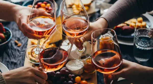Różowe wino, czyli alkohol etylowy w jedzeniu, w kieliszkach na tle serów, owoców i przekąsek.