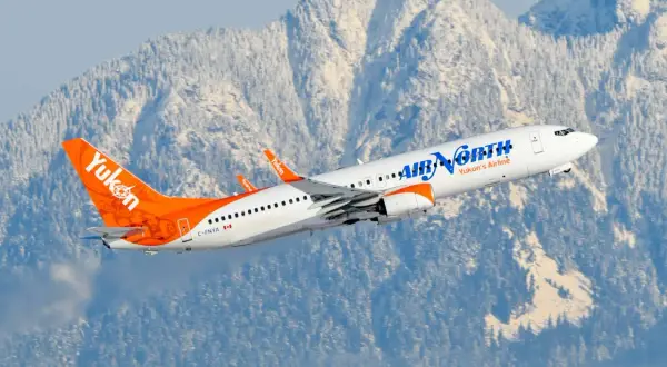 Boeing 737-900 linii Air North z charakterystycznym ogonem w barwach Yukon wzbija się na tle ośnieżonych gór.