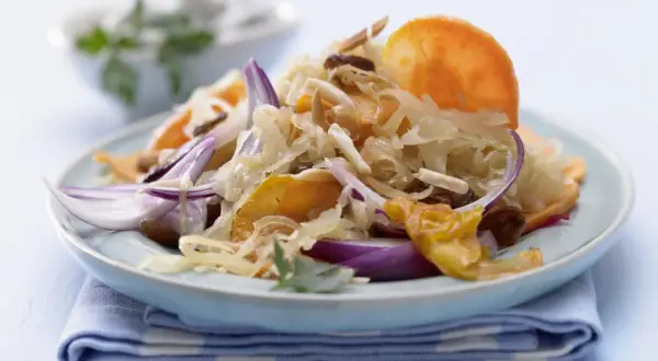 Ein Teller mit gebratenem Sauerkraut, garniert mit roten Zwiebeln, Rosinen und Mandelsplittern.