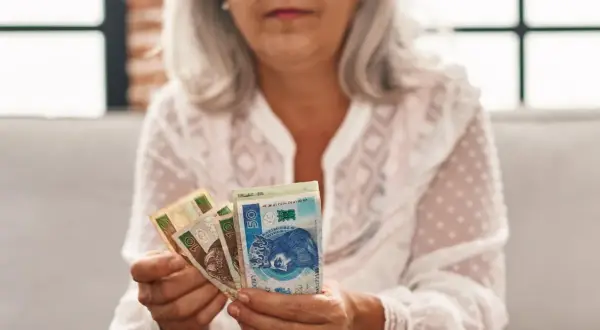 Kobieta z siwymi włosami trzyma polskie banknoty. To symbol oszczędności na emeryturę kapitałową dla kobiet.