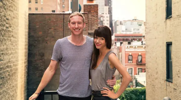 Jessica Walsh and her partner, perhaps celebrating a milestone in her most famous work, stand on a rooftop with a city skyline behind them.