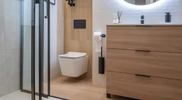 Modernos baños blancos y madera clara, con ducha de cristal, inodoro suspendido y mueble de cajones.