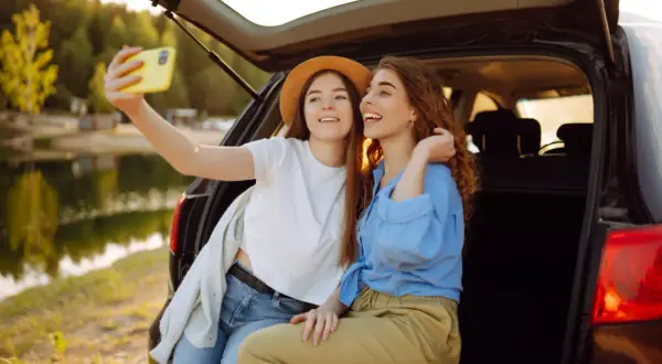 Dwie przyjaciółki robią sobie selfie przy samochodzie nad jeziorem. Idealny weekend z przyjaciółką!