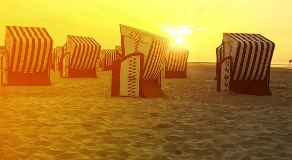 Zachód słońca nad plażą na Morzu Północnym w Niemczech. Puste kosze plażowe czekają na gości.