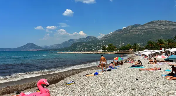 Plaża w Barze, Czarnogóra. Słoneczny dzień, ludzie odpoczywają na kamienistej plaży, a w tle widać góry. Atrakcje turystyczne tego miejsca przyciągają wielu wczasowiczów.