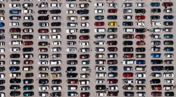 Wielki parking pełen europejskich marek samochodów, uporządkowanych w rzędy.