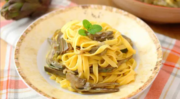 Tagliatelle fresche con carciofi teneri, guarnite con menta. Un piatto primaverile che celebra i sapori della terra.