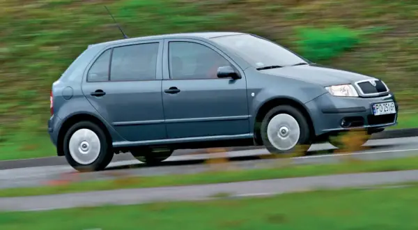 Szara, nowa Skoda Fabia pędzi po mokrej drodze, rozmazując zielone tło.