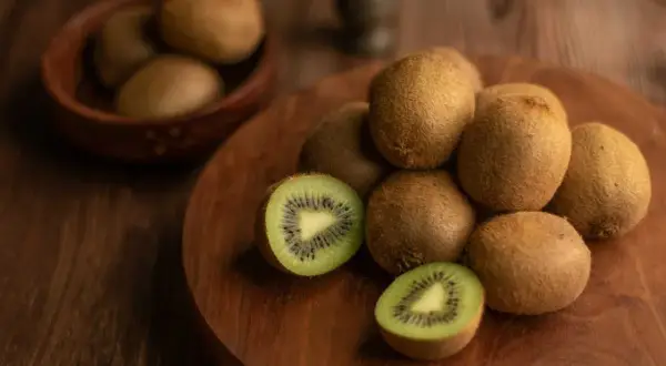 Kiwi, noti per essere tra i cibi che fanno andare in bagno, sono disposti su un tagliere di legno. Uno è tagliato a metà, mostrando la polpa verde e i semi neri.