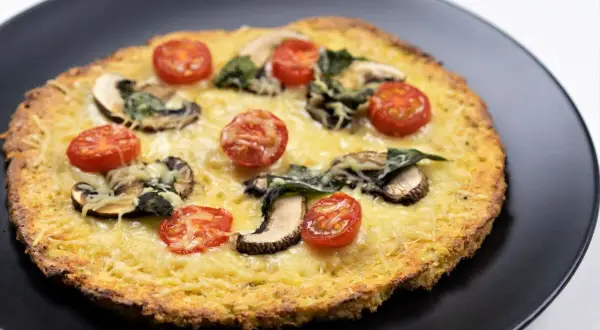 Deliciosa pizza de coliflor con queso derretido, champiñones y tomates cherry.