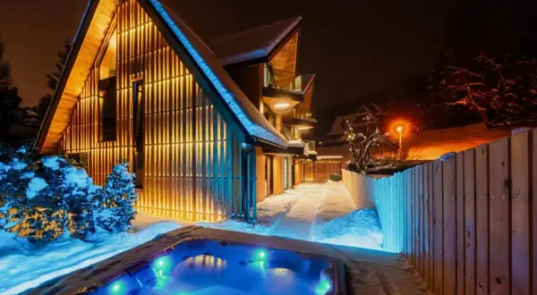 Nowoczesny dom w Zakrzewie oświetlony ciepłym światłem, z podświetlanym jacuzzi w śnieżnej scenerii.