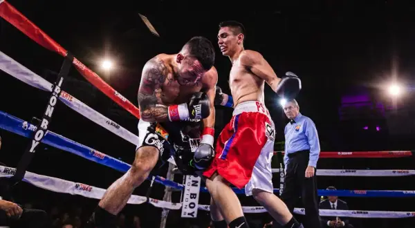 Två boxare i ringen, en med tatueringar, kämpar intensivt. Domaren ser på. Intensiv boxning för barn.