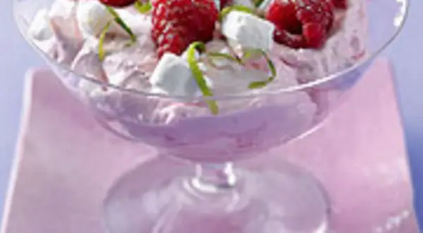 Himbeer-Mascarpone-Creme in einem Glas, garniert mit frischen Himbeeren, kleinen weißen Baiserstückchen und Zitronenmelisse.