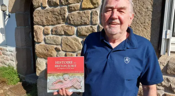 Un homme souriant tient un livre sur l'histoire du breton écrit. Son nom de famille breton est Favreau.