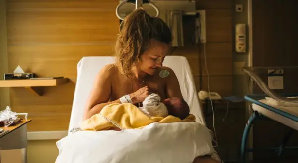 Nybliven mamma ammar sitt barn på en sjukhussäng. En lugn stund efter förlossningen, kanske inför en efterkontroll på MVC.