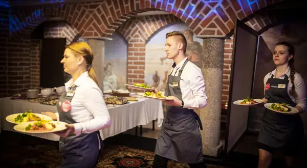 Kelnerzy niosą talerze z jedzeniem. Zastanawiasz się, jak się ubrać na kolację all inclusive? Elegancko, ale wygodnie, jak obsługa.