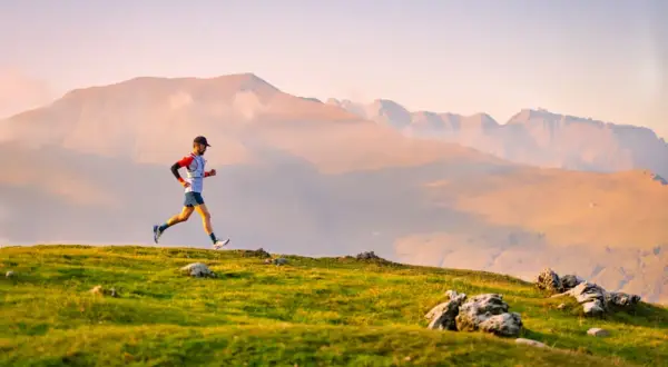 Un coureur en plein effort sur un sentier de montagne, prêt pour une ultra trail distance. Le soleil couchant illumine le paysage.
