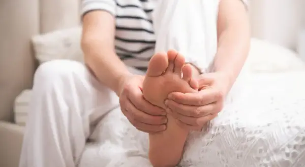 Osoba masuje stopę, odczuwając ból związany z neuropatią cukrzycową.