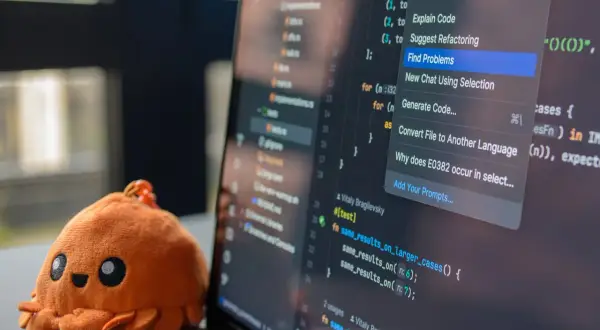 Un adorable crabe en peluche à côté d'un écran d'ordinateur affichant du code. Le menu contextuel propose des actions IA, aidant à choisir quel langage de programmation apprendre.