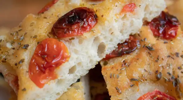 Nahaufnahme von Focaccia, einem der beliebtesten italienischen Brotsorten, mit getrockneten Tomaten und Kräutern bestreut.