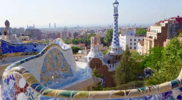 Bunte Mosaikbänke und Gaudís Märchenhäuser im Park Güell, eine der berühmtesten Barcelona Attraktionen, mit Blick auf die Stadt.