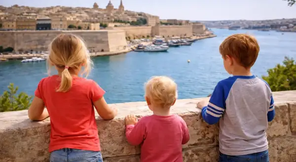 Drei Kinder blicken auf die Bucht von Valletta, Malta. Ein kleiner Junge, der fast wie ein Baby wirkt, steht in der Mitte.