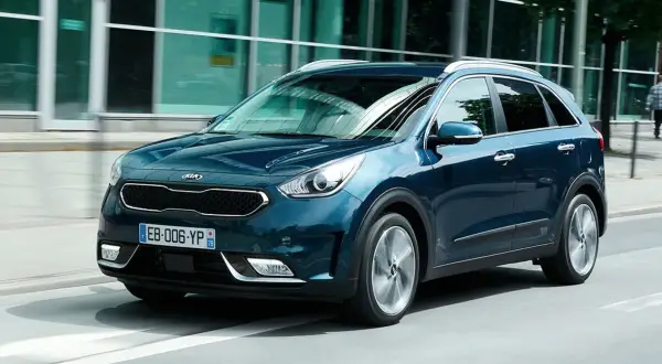 Ciemnoniebieski Kia Niro jedzie ulicą obok nowoczesnego budynku.