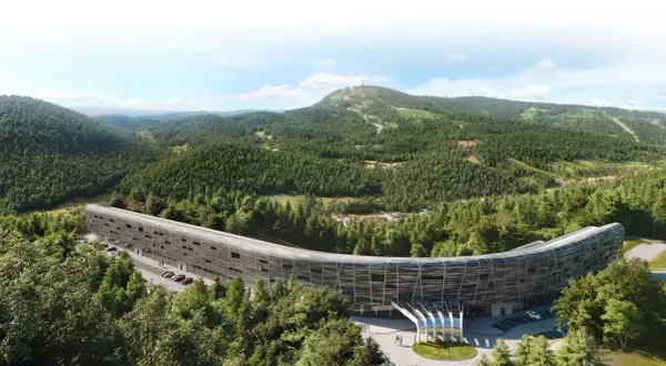 Nowoczesny, zakrzywiony budynek hotelu Mercure Szczyrk Resort otoczony lasem i górami.