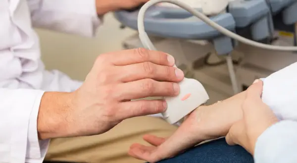 Lekarz wykonuje usg nadgarstka pacjenta, używając sondy aparatu do ultrasonografii.