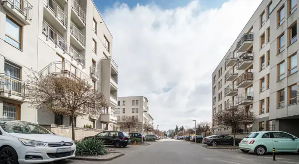 Nowoczesne bloki mieszkalne na osiedlu Zielona Italia, z balkonami i parkingiem pełnym samochodów.