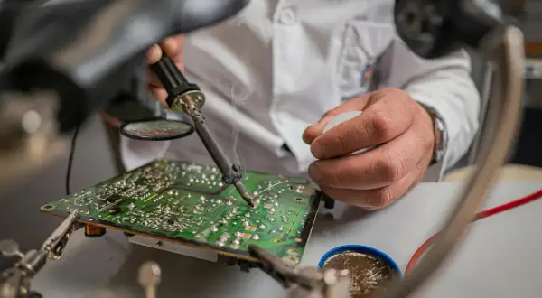 Ręce technika lutują płytę główną pod lupą. Nawet w **zimne luty** praca wre, by naprawić elektronikę.