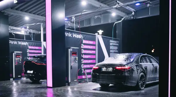 Nowoczesna bezdotykowa myjnia samochodowa Pink Wash nocą. Czarne samochody pokryte pianą, lśniące od wody podłogi i neonowe światła tworzą futurystyczny klimat.
