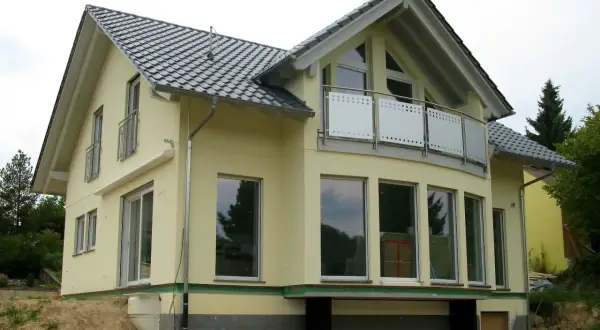 Nowoczesne projekty domów z poddaszem, żółty dom z dużymi oknami i balkonem, w trakcie budowy.