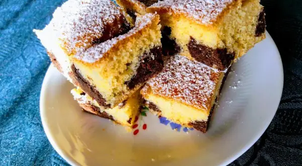 Ein saftiger versunkener Streuselkuchen mit Marmormuster, bestäubt mit Puderzucker, liegt auf einem Teller.