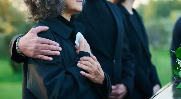 Odprawa pośmiertna: bliscy w żałobie, objęci ramieniem, trzymają chusteczkę.