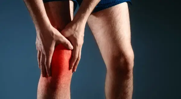 Mężczyzna trzyma się za zaczerwienione kolano, odczuwając nieprzyjemne szczypanie w kolanie.