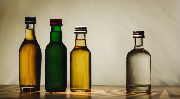 Cztery butelki z płynami: dwie z bursztynowym alkoholem, jedna z zielonym płynem i jedna z przezroczystym. Może to być domowy samogon.