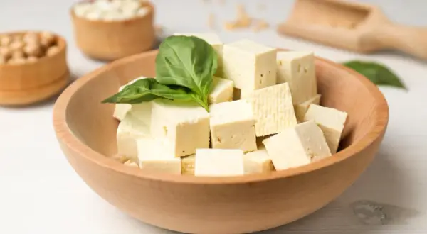 Kostki tofu w drewnianej misce, ozdobione listkiem bazylii. Czy tofu można jeść na surowo? Tak, to świetna baza do sałatek!
