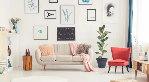 Sofa w kolorze ecru, jaki to kolor? Delikatny, przytulny, idealny do salonu. Obok niej czerwony fotel i mnóstwo obrazów na ścianie.
