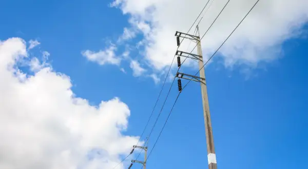 Słupy energetyczne na tle błękitnego nieba z chmurami. Widać przewody i izolatory. Określenie odległości słupa energetycznego od granicy działki jest kluczowe dla bezpieczeństwa.