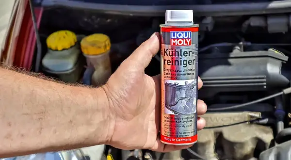 Ręka trzyma puszkę preparatu do płukania układu chłodzenia Liqui Moly. W tle widać silnik samochodu.