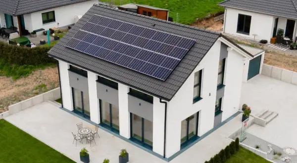 Nowoczesny biały dom z panelami słonecznymi na dachu, tarasem i ogrodem.