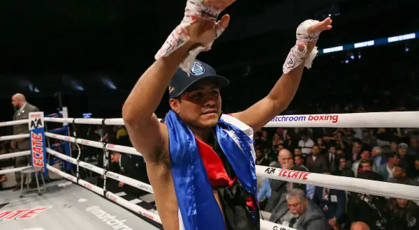 A victorious boxer, representing Nicaraguan pride, raises his taped hands in triumph in a packed arena.