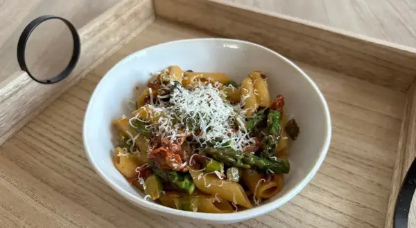 Makaron penne z zielonymi szparagami i suszonymi pomidorami, posypany parmezanem.