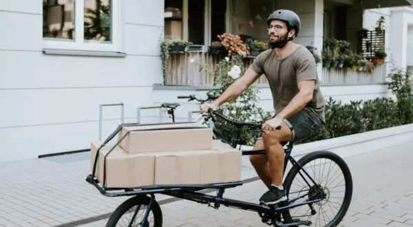 Mann liefert Pakete mit einem Lastenrad. Eine gute Lastenrad Versicherung schützt vor unerwarteten Schäden.