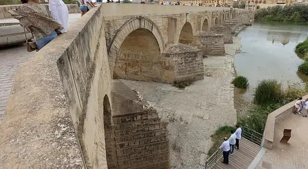 Gente admira el puente romano de Córdoba. Para llegar, sigue el río Guadalquivir.