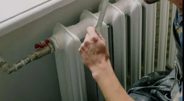 Mano che misura il detentore del termosifone con un righello.