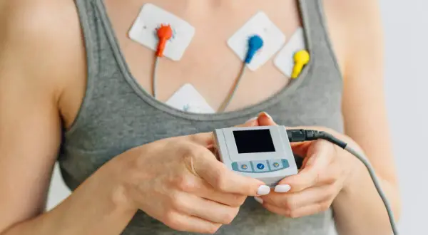 Kobieta z elektrodami na klatce piersiowej i małym urządzeniem do monitorowania EKG. Przygotowanie do badania EKG.
